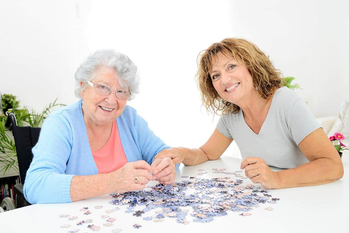 Barton House Memory Care | Senior woman and caregiver smiling and doing a puzzle