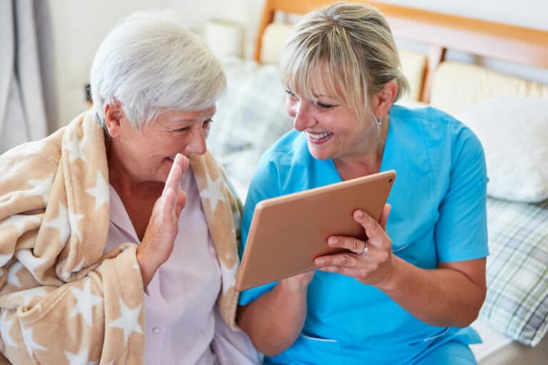 Novellus Cypresswood | Senior woman waving to an iPad held by her caregiver