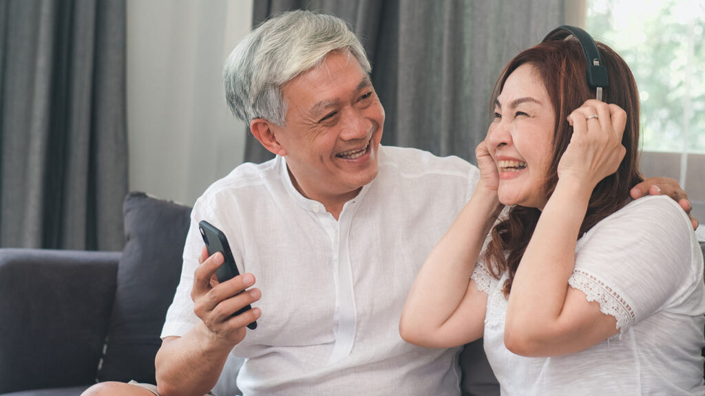 Novellus Kingwood | Asian senior couple relax at home. Asian Senior Chinese grandparents, husband and wife happy wear headphone using mobile phone listen to music while lying on sofa in living room at home concept.