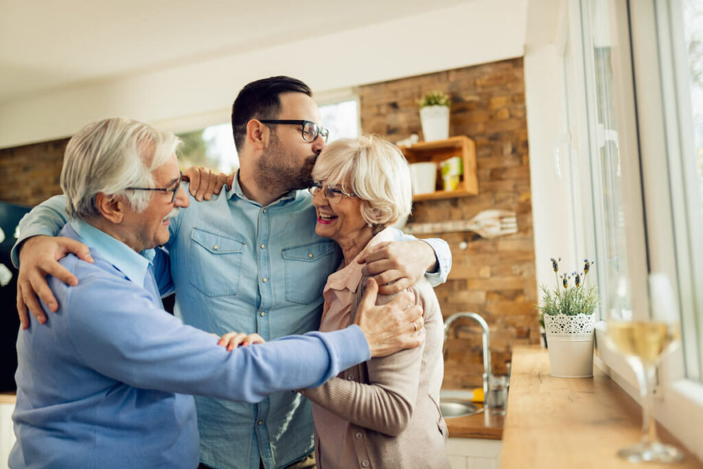 Stockton Assisted Living | Adult son and his senior parents hugging and smiling in the kitchen