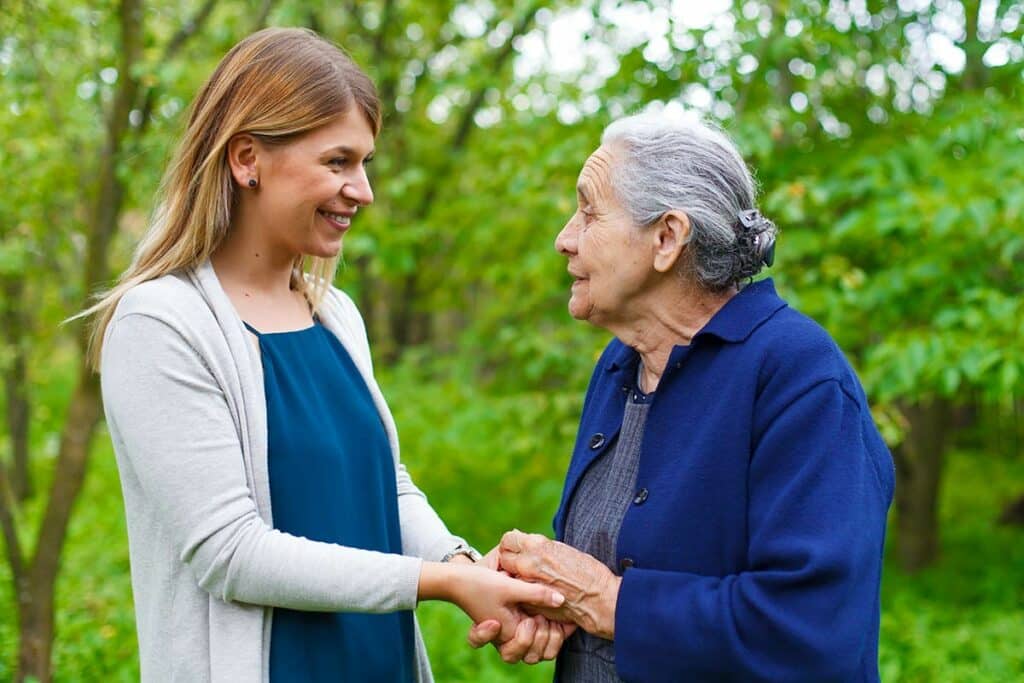 Orangeburg Memory Care | Senior woman and caregiver holding hands outside